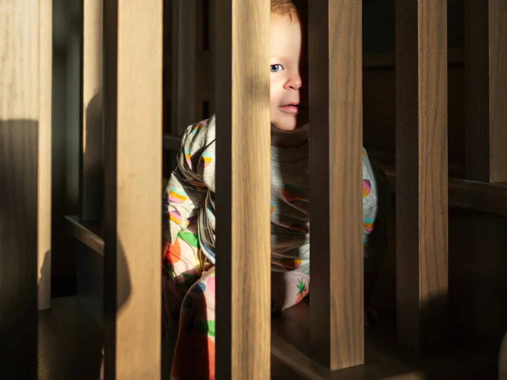 Kind kijkt tussen de spijlen van een trap door