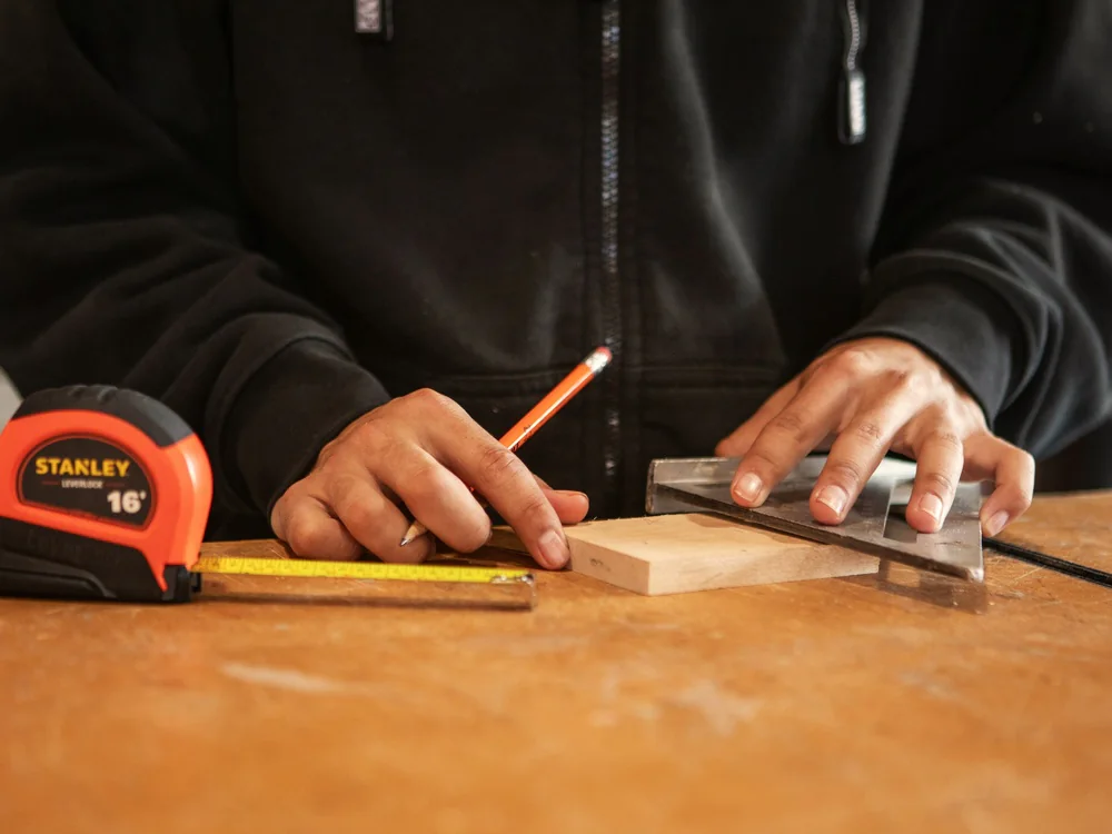 Vakman tekent een maat af op een plank met rolmaat en winkelhaak